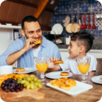A father and son share breakfast together in a well-lit kitchen. 